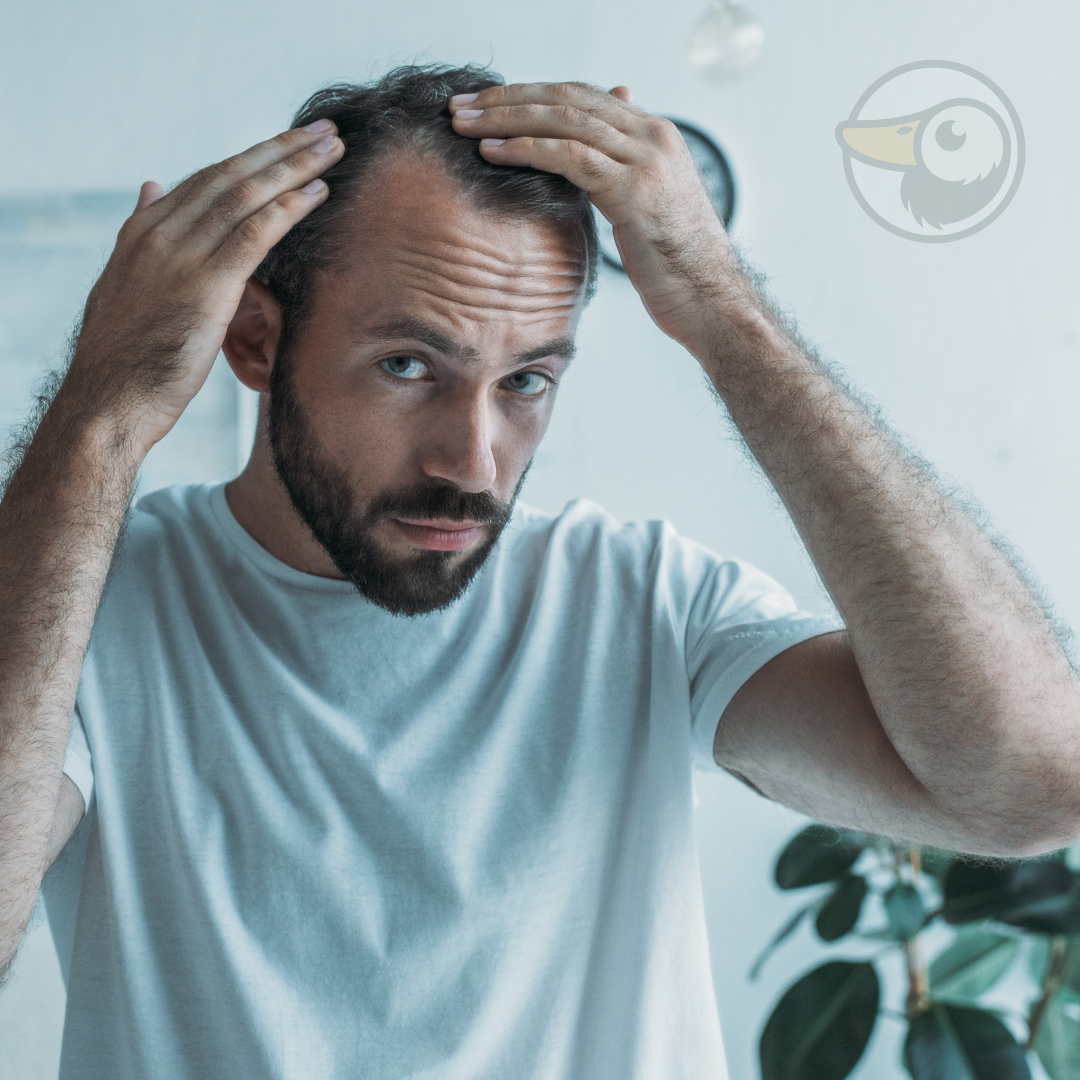 Man with a full beard looking worryingly at receding hairline in mirror