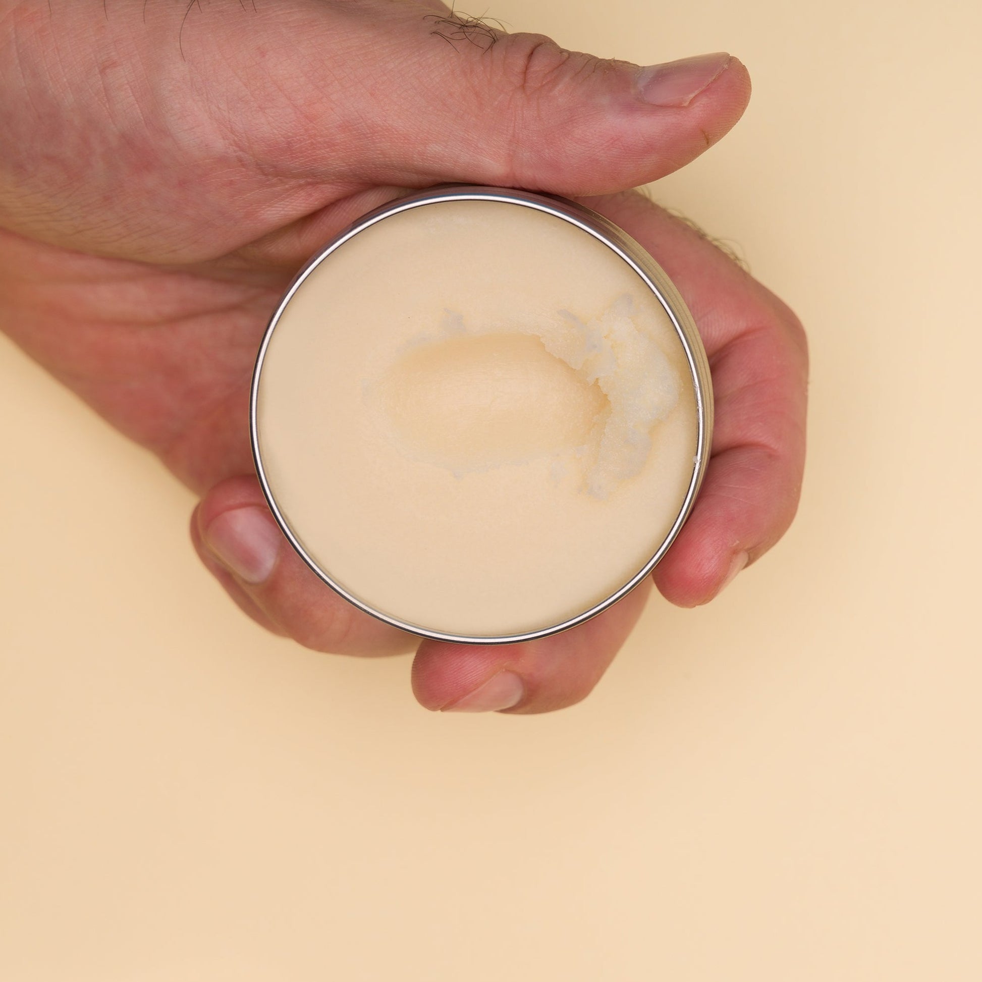 Hairy As Beard Love Beard Butter blend Juicy Bush held in a left hand. The bottom half of an open 60ml grey aluminium screw top tin to show the beard butter inside. A scoop has been taken out of the butter.