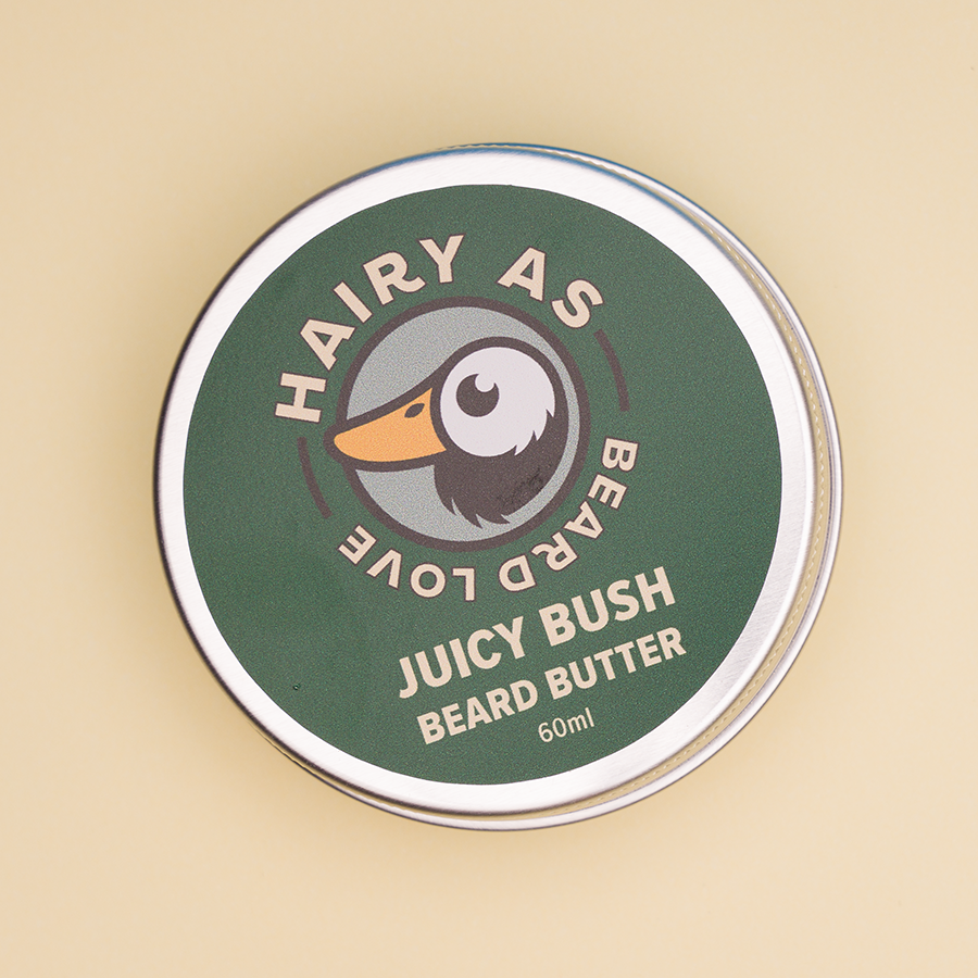 Hairy As Beard Love Beard Butter blend Juicy Bush. A 60ml grey aluminium screw top tin. Label is green with cream coloured font. Features the Hairy As logo of a bearded duck.