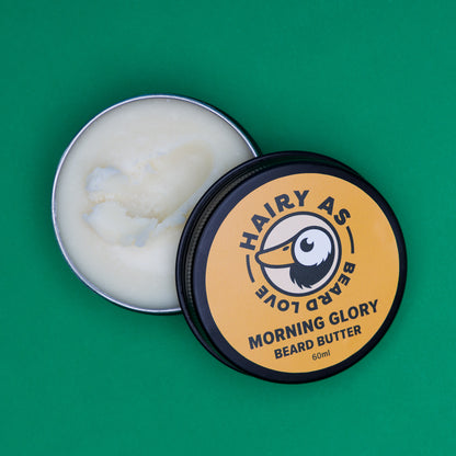 Tin of Hairy As Morning Glory Beard Butter open on a green surface. Image some has been taken from tin which highlights its creamy texture and natural ingredients for optimal beard care.