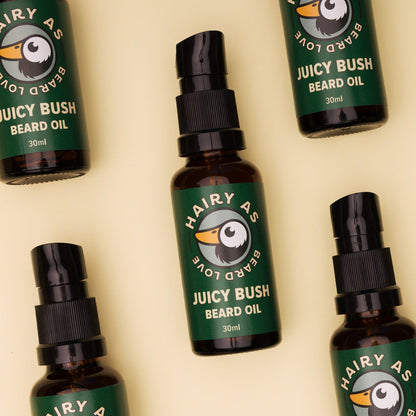 Hairy As Beard Love Beard Oil blend Juicy Bush. A 30ml amber glass bottle with a black serum pump cap, one complete bottle showing along with 4 more part showing. Label is green with cream coloured font. Features the Hairy As logo of a bearded duck. Jasmine background.