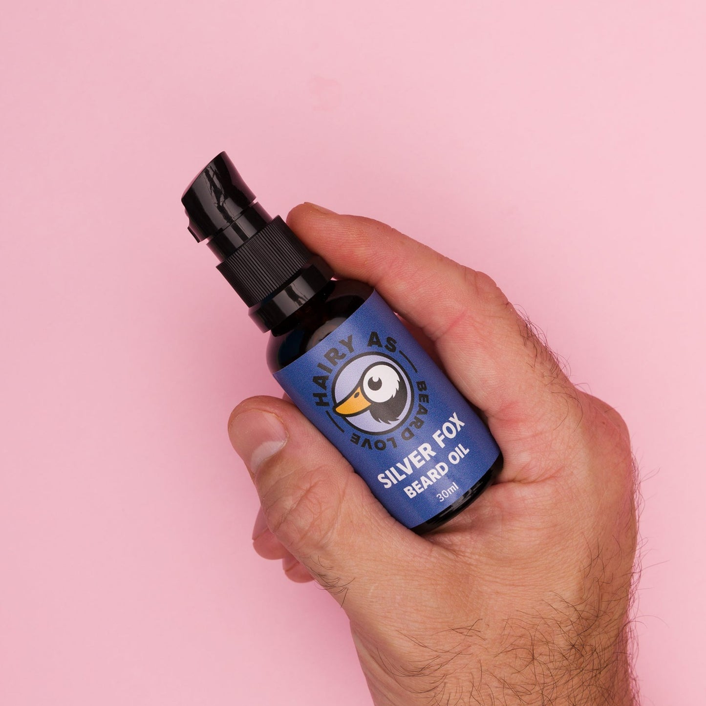 Bottle of Hairy As Silver Fox Beard Oil being held in a right hand with a piunk background, emphasizing its elegant packaging and premium quality for beard grooming.